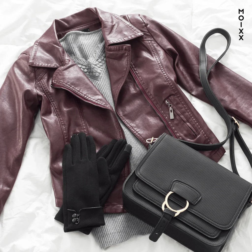 Conjunto de moda con chaqueta de cuero burdeos, suéter gris, guantes negros y bolso negro sobre fondo blanco