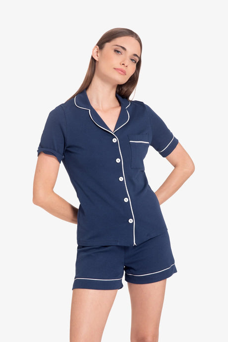 Mujer con pijama azul marino de manga corta y pantalones cortos con ribetes blancos en fondo blanco