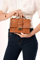 Bolso de mano marrón de cuero con cierre metálico dorado sostenido por mujer con blusa blanca y pantalones vaqueros