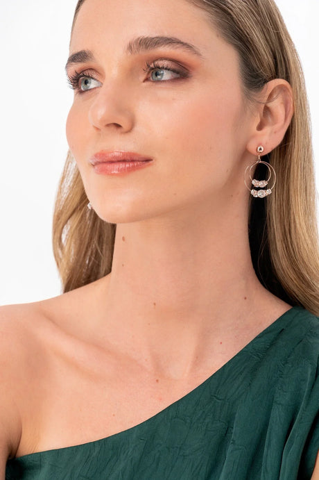 Mujer con maquillaje natural, pendientes dorados con cristales y vestido verde de un solo hombro