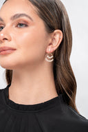 Mujer con pendientes dorados con diseño de hojas y blusa negra elegante en fondo blanco