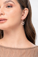 Perfil femenino con aretes colgantes de cristal y pendiente pequeño en ambiente neutro