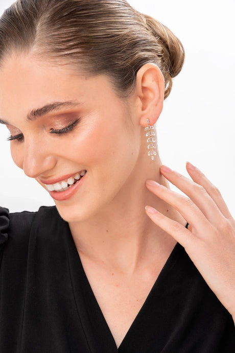 Mujer con pendientes colgantes dorados en forma de hojas, vestida con blusa negra y piel luminosa