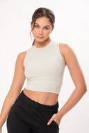 Mujer joven con top sin mangas blanco y pantalones negros posando con fondo blanco