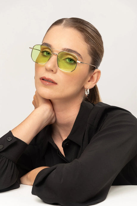 Mujer con gafas de sol estilo vintage de lentes amarillas y armazón metálico, camisa negra y aretes plateados