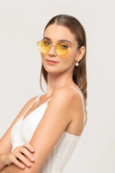Mujer con gafas amarillas y vestido blanco de tirantes posando en fondo claro
