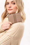 Mujer rubia con suéter beige sosteniendo cartera marrón con textura y cierre dorado