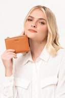 Mujer rubia con camisa blanca mostrando cartera pequeña de piel color marrón con logo MOIXX