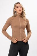 Mujer con chaqueta deportiva beige de cremallera y leggings oscuros, fondo blanco